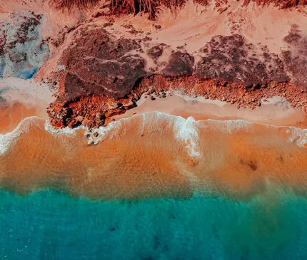Vivid Red Rockface Adjacent To Blue Ocean In Broome Western Australia