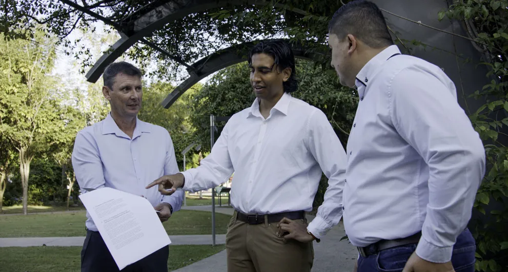 Indigenous Outcomes staff talk with CEO of NAIF holding Strategy Toolkit documents in Martin Munroe Park
